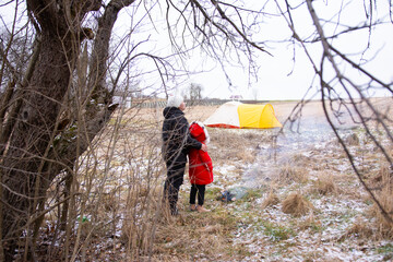 Exploration and warmth in a winter landscape with a bright tent and two figures embracing amidst nature's chill at an outdoor campsite