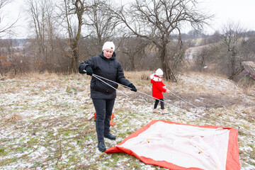 Setting up a winter camping tent on a snowy hillside with family enjoying quality time outdoors in a serene landscape