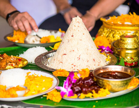 A conical mound of rice, surrounded by various dishes and flowers, is being served during a ceremony.
