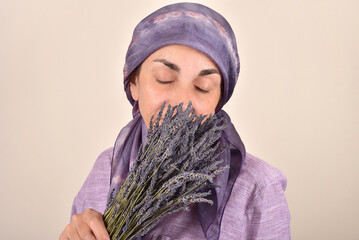 Mature woman with closed eyes and scarf on her head holding and smelling bouquet of lavender flowers