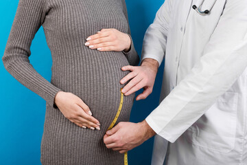 happy beautiful pregnant young woman touching her bare tummy while a doctor is measuring it