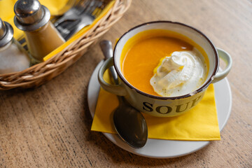 Rustic-style pumpkin cream soup served in a vintage metal bowl with chipped enamel and the word soup printed on it, placed on a wooden table with yellow napkin and cutlery in cozy cottagecore setting