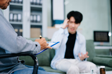 Obraz premium Young Asian man discusses mental health with psychiatrist in office. Emotional support, anxiety, therapy, and compassionate care.