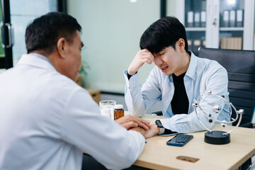 Young Asian man discusses mental health with psychiatrist in office. Emotional support, anxiety, therapy, and compassionate care.