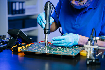 Senior technician soldering a circuit board on workbench. Blue gloves, precision tools, and...