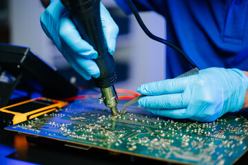 Senior technician soldering a circuit board on workbench. Blue gloves, precision tools, and...