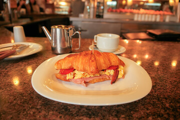Plate of savoury breakfast croissant with scrambled eggs ham cheese tomato bacon in a cozy diner setting cafe setting. Shot in famous restaurant cafe in Asunción, Paraguay. Desayuno. Selective focus.