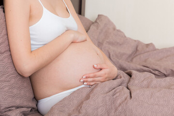 Young pretty pregnant woman, in pain, sitting on bed in bedroom, preparing to give a birth