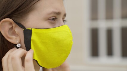 A young girl in a mask is having fun talking on a smartphone online and laughing, modern life of...
