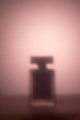 A blurred silhouette of a perfume bottle set against a soft pink gradient background abstract fragrance and beauty concept