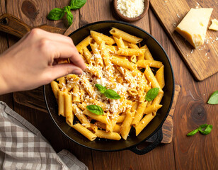 A person sprinkles grated cheese over a pasta dish, ready to eat.
