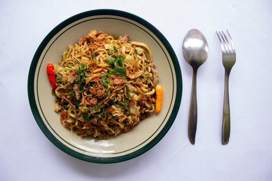 "Mie Goreng Jawa or bakmi jawa or java noodle with spoon and fork. Indonesian traditional street food noodles from central java or Yogyakarta, indonesia on white background."