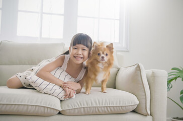 Portrait of little asian girl stay home sit on the sofa  living room with lovely dog. Happy moment of pure love toddler playing with little dog, minimal happy pet animal lifestyle concept