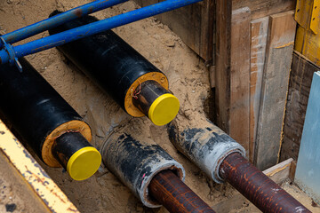 Construction workers are installing utility pipes in a deep trench filled with sand. The pipes are...