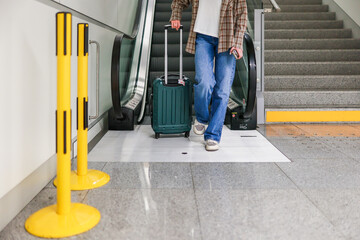 A young woman steps off the escalator at an airport, with only her legs and suitcase visible. The image captures a dynamic travel moment, highlighting movement and the flow of modern transit. 