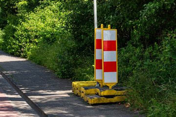 Bright yellow and red construction barriers are positioned on a sidewalk, surrounded by lush...
