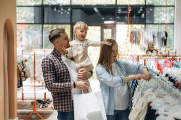 Bunch of wear hanging. Father, son and pregnant mother are in kid's clothing store
