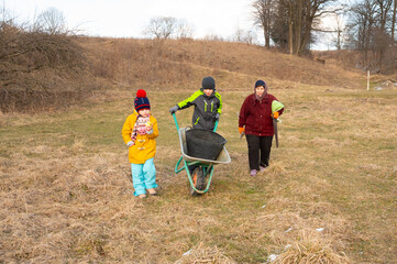 Family members working together in a field during a chilly day, transporting items with a wheelbarrow in a beautiful rural landscape