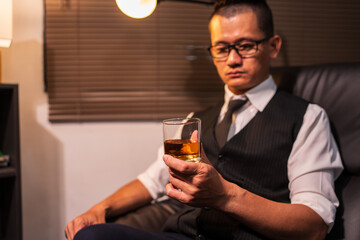 Businessman holding a glass of whiskey and drinking on a sofa.