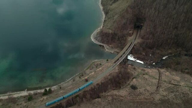 A spring landscape of Lake Baikal with a view of clearwater and a railway with a train at the foot of the hills