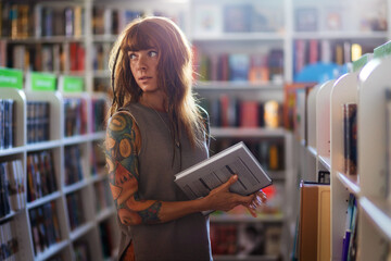Looks around young Caucasian woman with tattoo holds book in bookstore. Concept of education and...