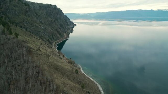 A spring landscape of Lake Baikal with a view of clearwater and a railway with a train at the foot of the hills