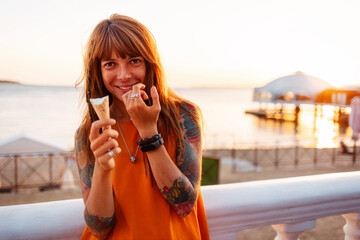 Portrait of young happy beautiful Caucasian woman with tattoos holds ice cream and looking at...