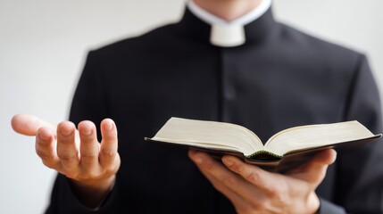 Christian priest in black clerical robe holding open bible with one hand and gestu with the other