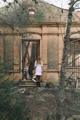 Woman standing with eyes covered by the hair next to the abandoned house