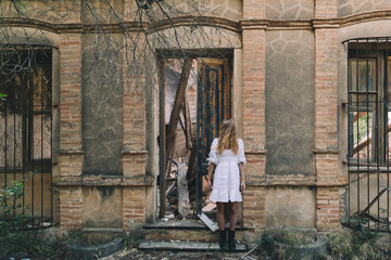 Woman standing with eyes covered by the hair next to the abandoned house