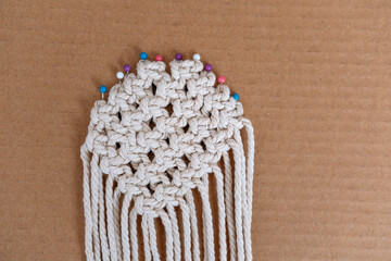Round pinned macrame piece with colorful pins on cardboard background
