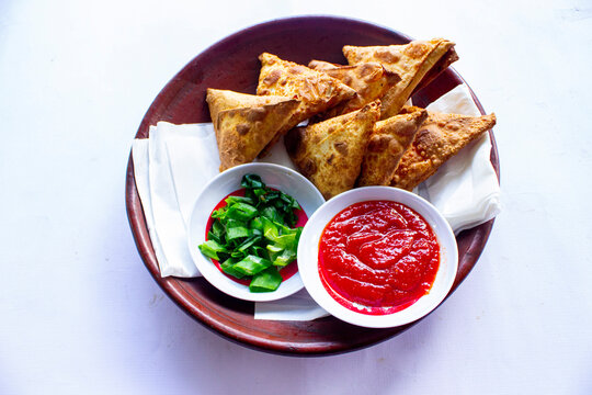 Samosa, samsa or somsa are triangular fried pastries or pastri served with tomato sauce and leek slice, on black background