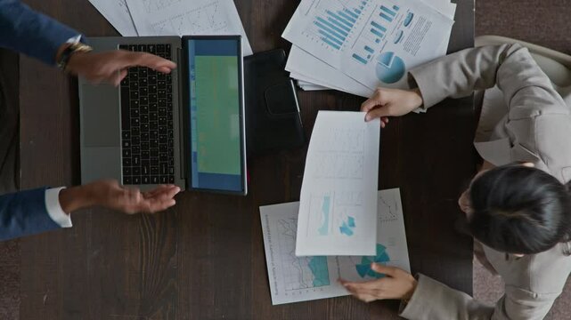 Top view of male company boss reviewing financial report prepared by junior female business analyst on laptop computer, then praising her work and shaking hands