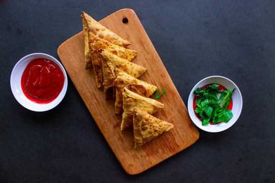 Samosa, samsa or somsa are triangular fried pastries or pastri served with tomato sauce and leek slice, on black background