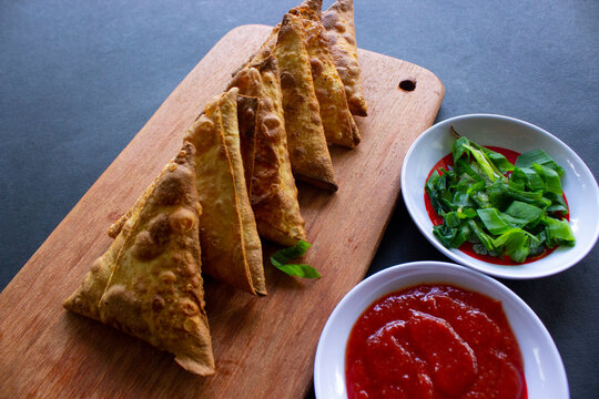 Samosa, samsa or somsa are triangular fried pastries or pastri served with tomato sauce and leek slice, on black background