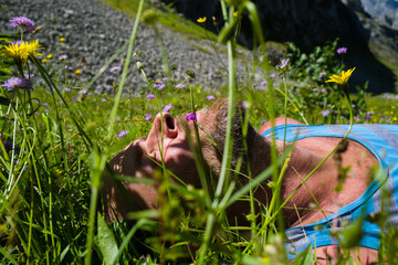 Man laying on grass holding a flower in his mouth