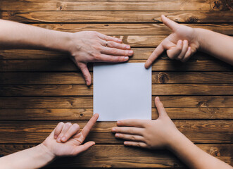 A white sheet of paper lies between the hands of a young girl and a little girl. The knotted...