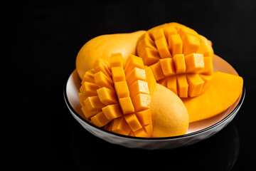 A white bowl holds vibrant yellow mangoes, some diced into perfect cubes, others whole.
