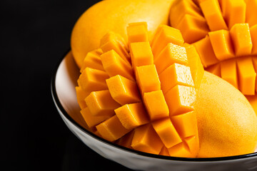 A white bowl holds vibrant yellow mangoes, some diced into perfect cubes, others whole.