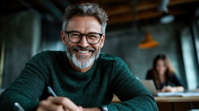 This cheerful portrait features a mature man with a friendly smile, sitting at a desk, symbolizing wisdom, approachability, and a positive attitude in a collaborative work environment.