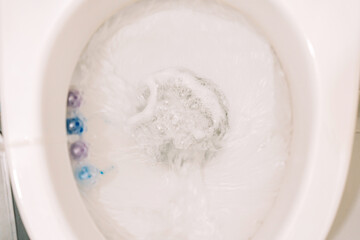 Close-up of toilet bowl during flushing with foam and water swirling, toilet freshener visible on the side. High quality photo