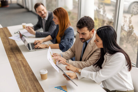 Gender balanced collective sitting at corporate office and analyzing charts and documents.