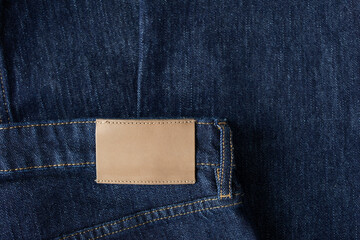Empty leather tag or label on blue denim jeans clothes top view. Shopping, sale and fabric industry background.