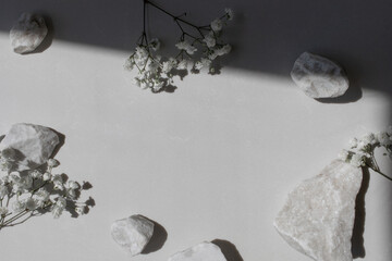 White decorated stones, gypsophila flowers and sunlight shadows on neutral background. Aesthetic composition for minimalistic spa template.