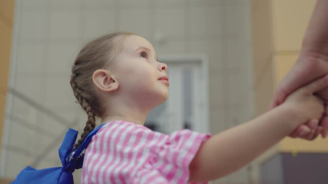 child rushes to school for lessons, little kid with school backpack holds his mother by hand, mom leads her daughter school, children's school life, happy family, bag on shoulders of schoolgirl girl.