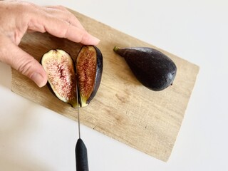 Hands slicing early fig fruit on table.