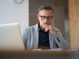 Thoughtful middle aged businessman working on laptop