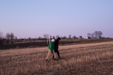 Two friends enjoy an evening stroll across the serene landscape of a rural field as the sky transitions into twilight during early spring
