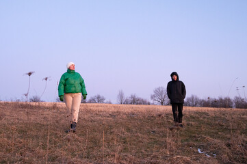 Twilight stroll across an open field with friends enjoying nature's tranquility and warm attire in early evening light, embracing the serene moment together