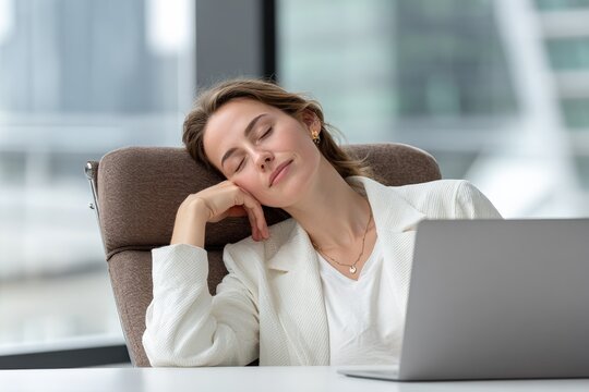 Young woman tired and sleeping at desk in modern office with laptop and large , feeling exhausted or drained du workday or break time